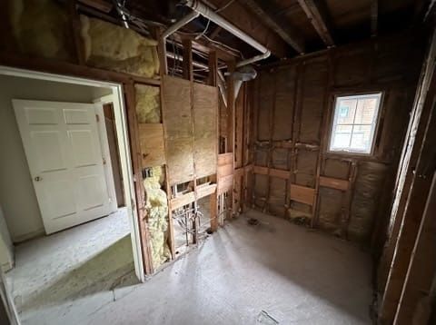 Partially gutted room with exposed wall framing, a small window, and a white door to the left.