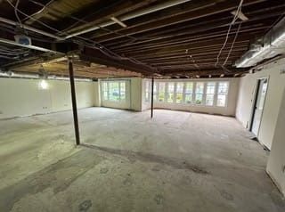 Empty unfinished basement with exposed ceiling joists, concrete floor, and windows along one wall