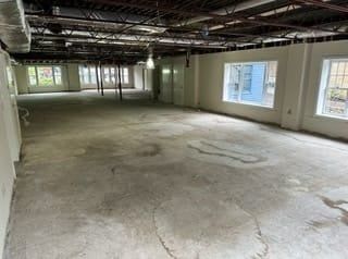 Empty unfinished room with concrete floor, exposed ceiling, and windows along the right wall.