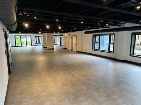 Empty modern office space with gray floor, white walls, black ceiling, and large windows