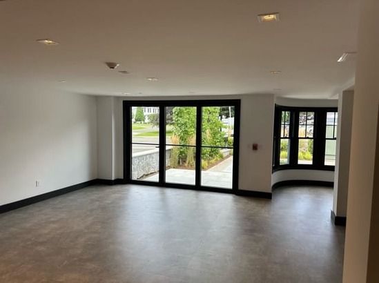 Empty modern room with tiled floor, recessed lights, and glass doors opening to a garden patio.