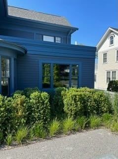 Blue house exterior with tall shrubs along a paved path under a clear sky