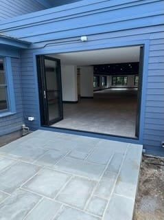 Blue house exterior with open sliding door leading to an empty interior room and concrete patio.