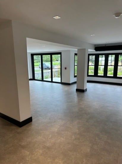Empty modern room with large windows, white walls, black trim, and light gray flooring.