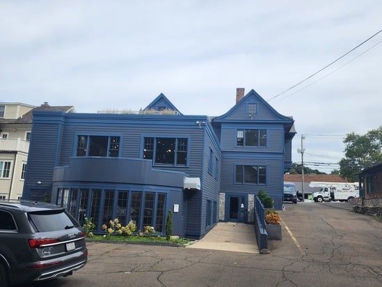 Blue two-story building with multiple windows and a parking area beside it
