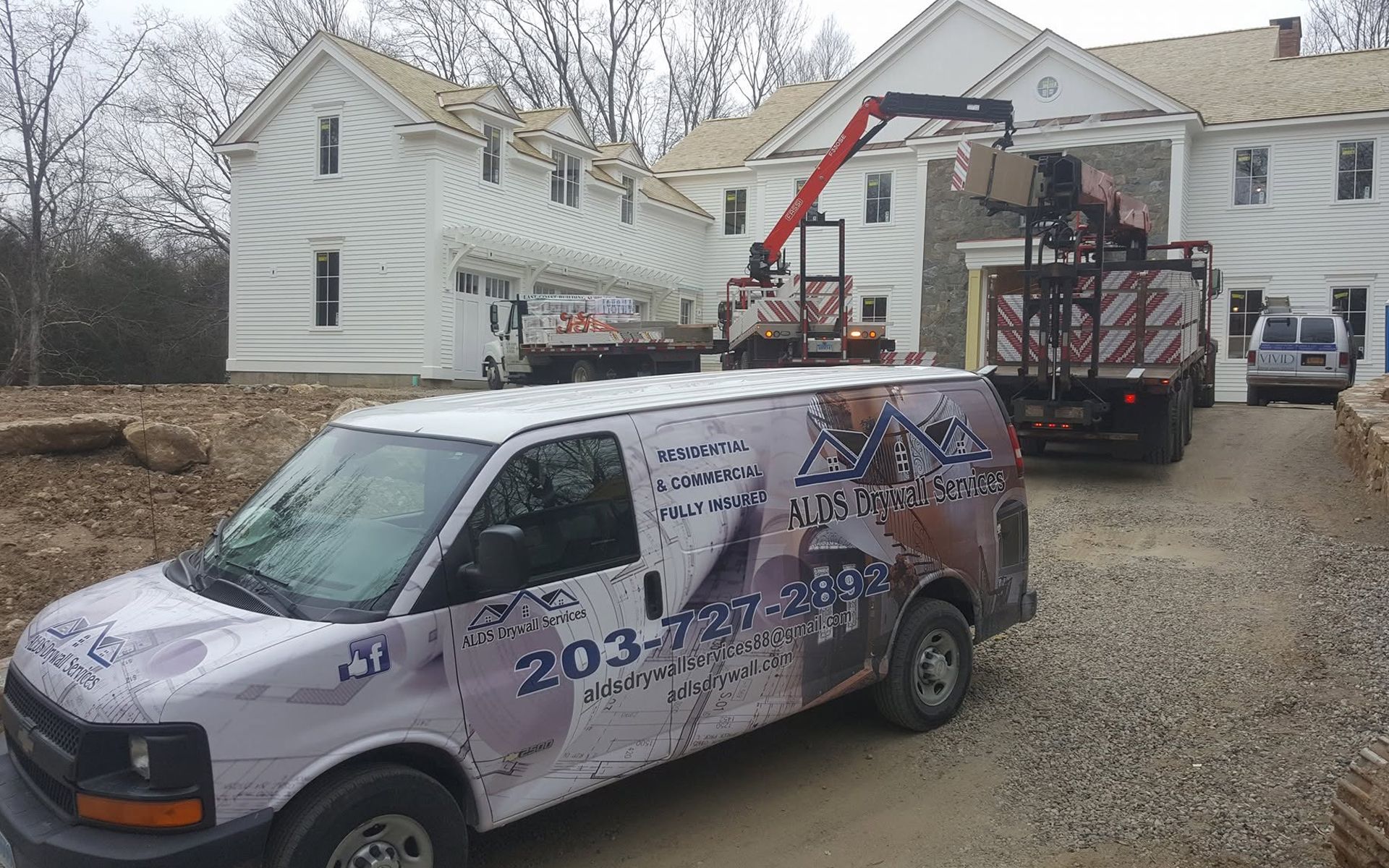 Work van and bucket lift truck parked outside a house under construction on a gravel driveway