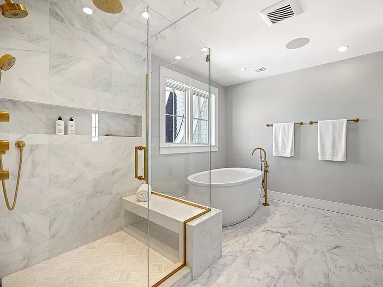 Luxurious marble bathroom with a gold shower, a freestanding tub, and a bench.