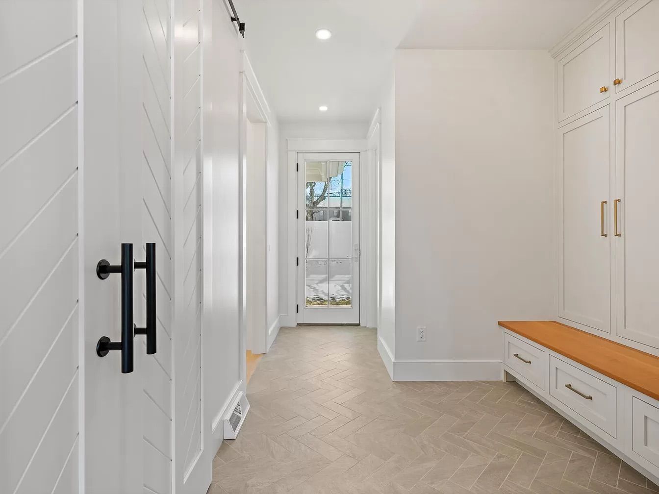 White hallway with herringbone floor, a barn door, storage cabinets, and a bench with a wood seat.