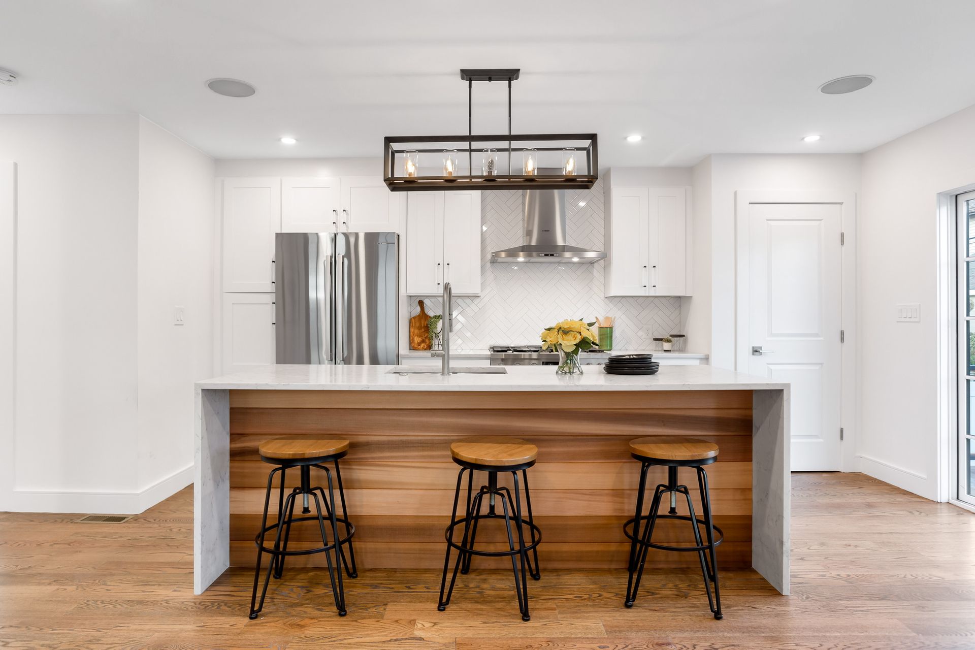Modern kitchen with white cabinets, wood accents, and a kitchen island with three stools.