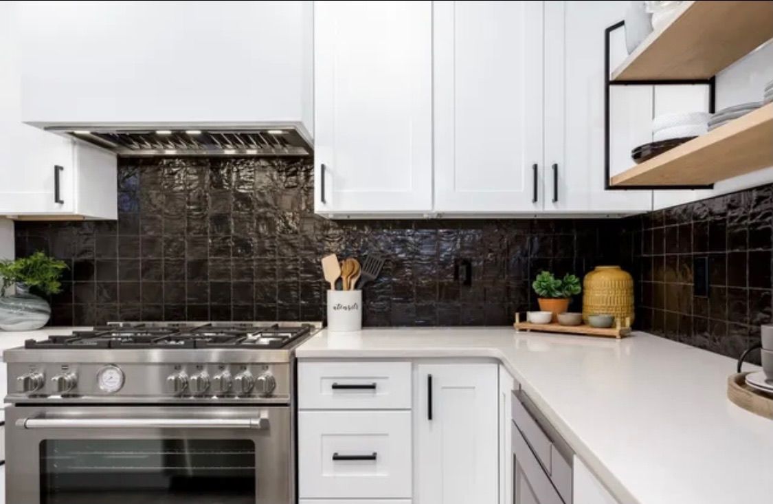 Modern kitchen with white cabinets, stainless steel appliances, black textured tile backsplash, and light countertops.