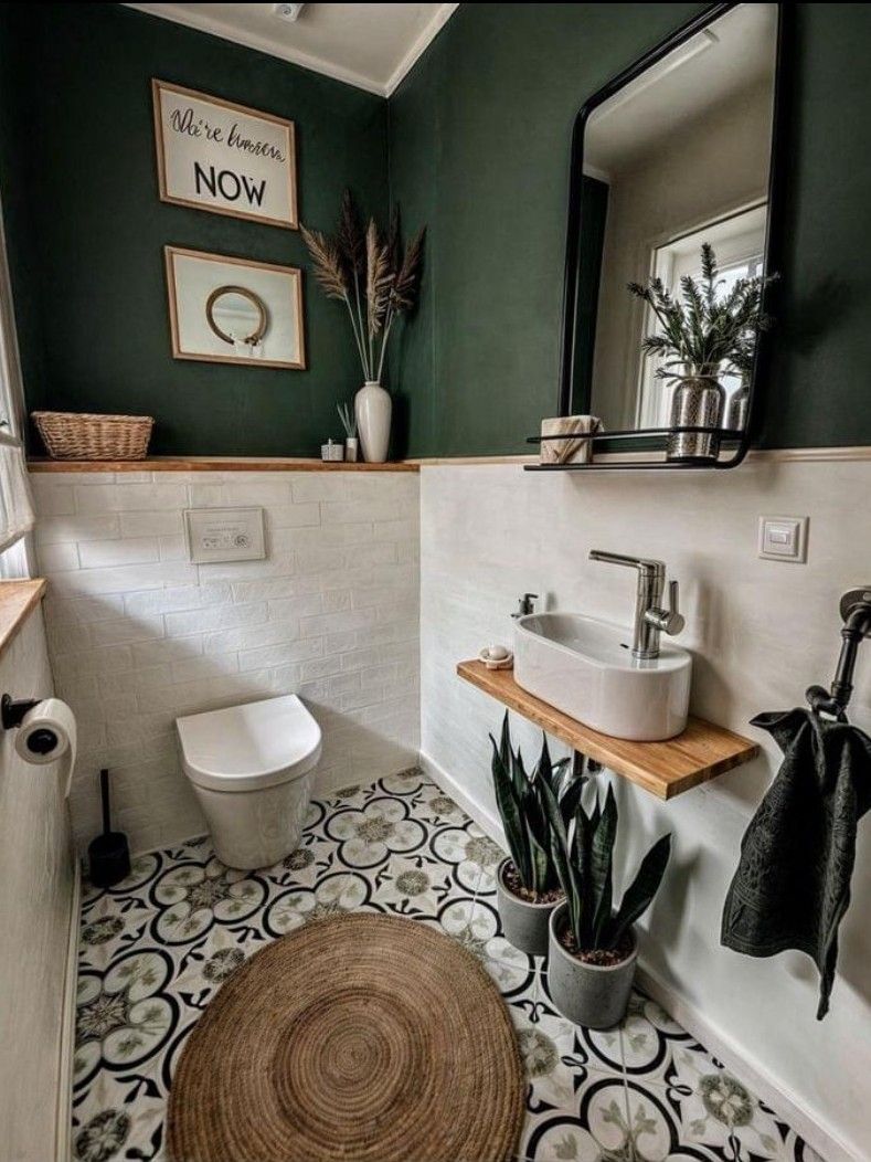 Small, modern bathroom with dark green upper walls and white tiled lower walls. Features include patterned floor tiles, a floating sink, and natural decor.