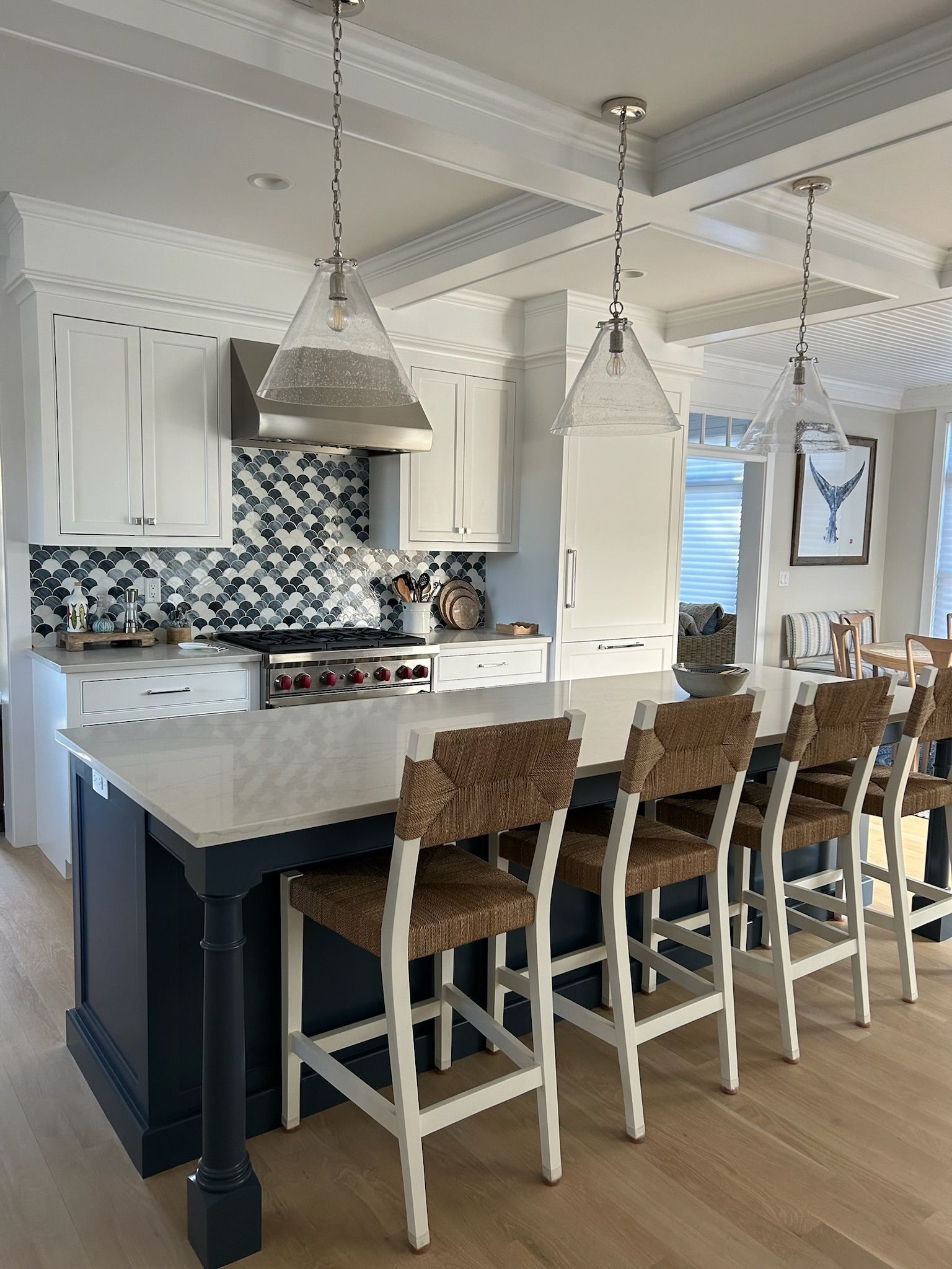 A kitchen with a large blue island and white cabinets. Bar stools with woven seats line the island. Three pendant lights hang above.