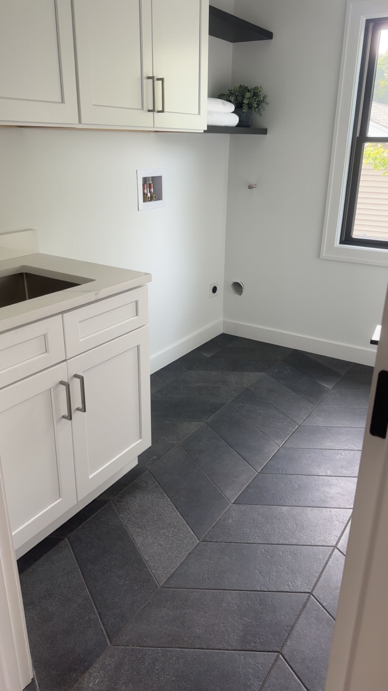 Laundry room with white cabinets and dark gray patterned floor. A sink and window are visible.