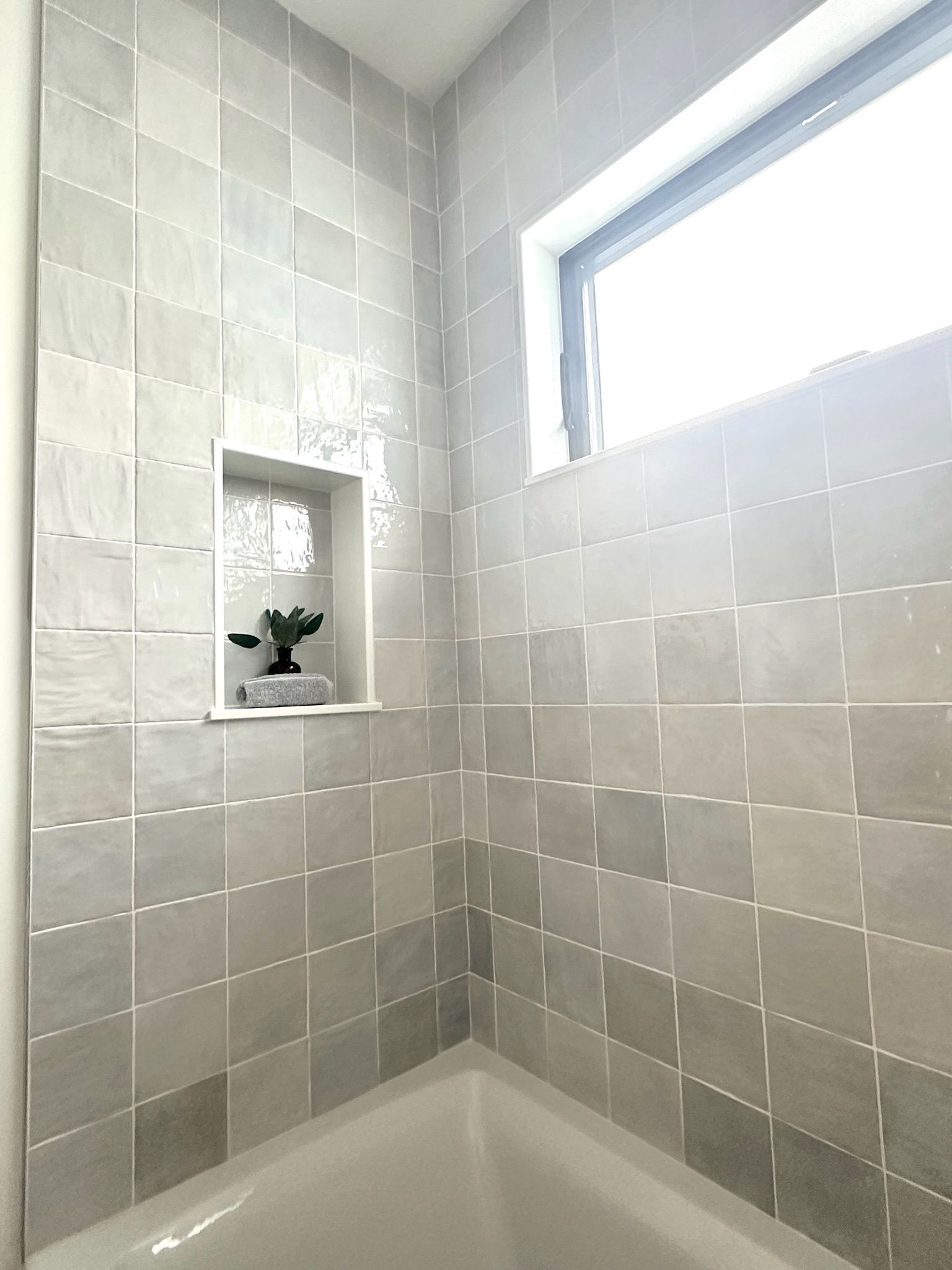 Bathroom with gray square tiles, a recessed shelf, and a small window. Bathtub is visible at the bottom.