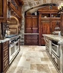 A luxurious kitchen with wooden cabinetry, stone floors, and a large island with a stainless steel oven.