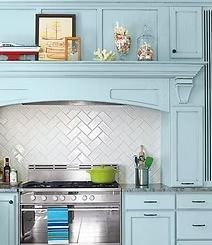 Blue kitchen with white herringbone backsplash and stainless steel stove.  Shell-filled jars and nautical decor sit on a shelf.