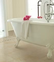 White claw-footed bathtub with a towel and pink flowers, set in a bright bathroom.