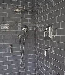 Gray tiled shower with chrome fixtures, including a showerhead, controls, and soap holder. 