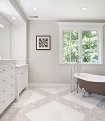 A modern bathroom with a bathtub in front of a window, white cabinetry, and patterned floor tiles.