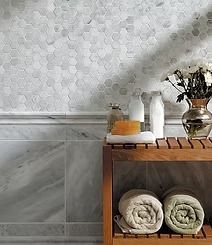 A bathroom with marble walls and a wooden shelf holding towels and toiletries. A vase of flowers sits on the shelf.