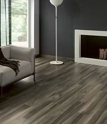 Modern living room with gray wood-look flooring, a light gray sofa, dark gray walls, a white floor lamp, and a white fireplace.