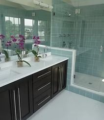 A modern bathroom with a dark wood vanity, double sinks, and a glass-enclosed shower. Light blue tiles and a white floor complete the space.
