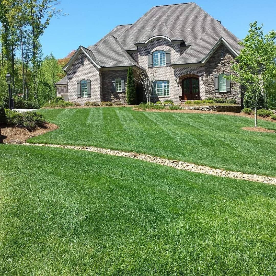 Large brick house with a well-manicured green lawn under a blue sky.