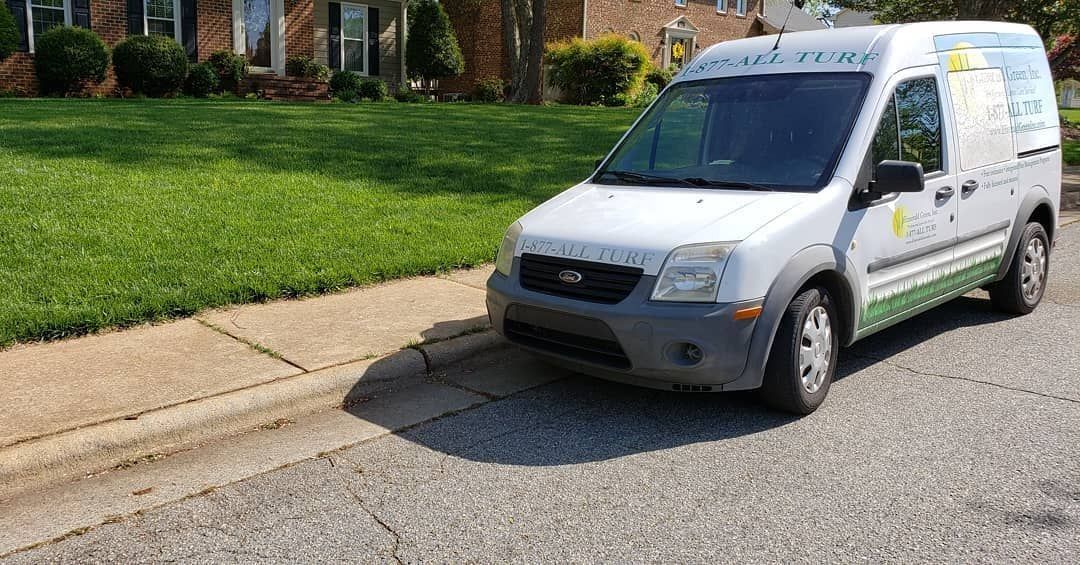 White van parked on a street next to a green lawn.
