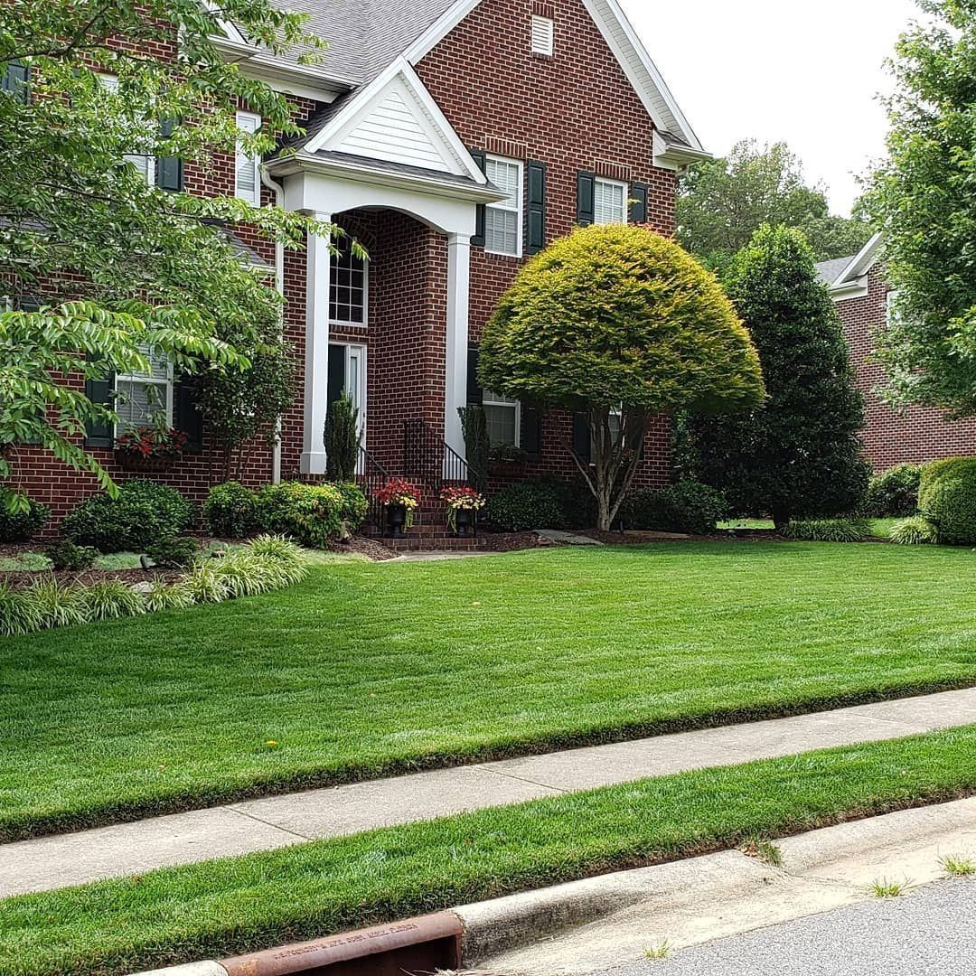 Brick house with green lawn, trimmed trees, and a sidewalk.