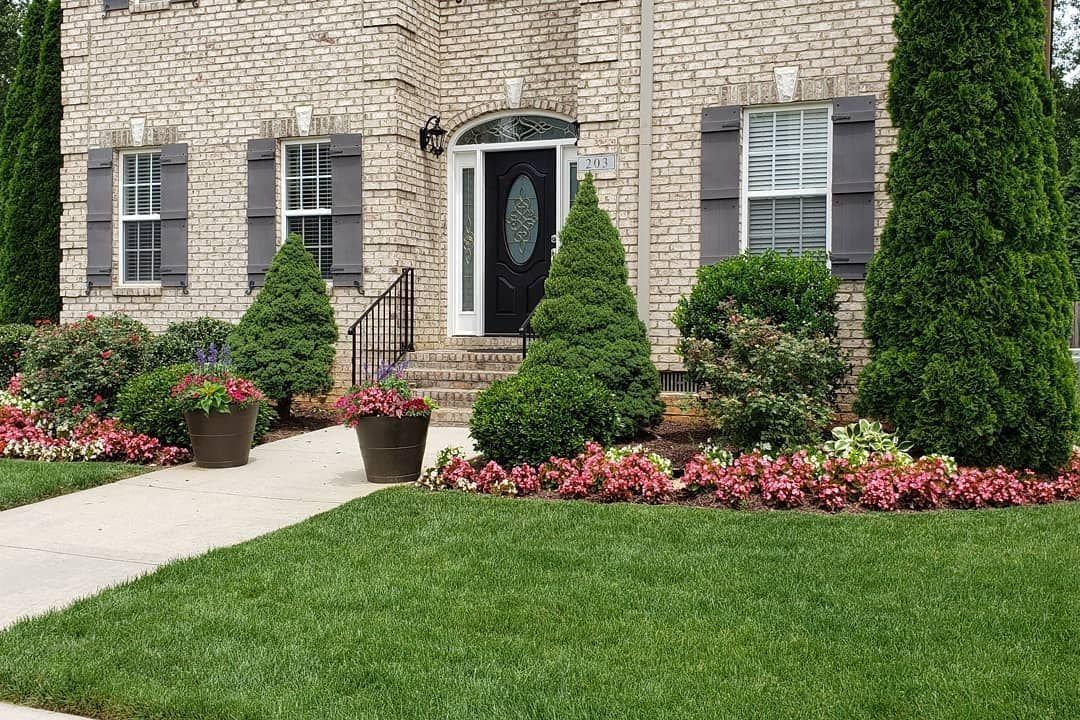 A brick house with a manicured lawn, flowerbeds, and a concrete walkway.