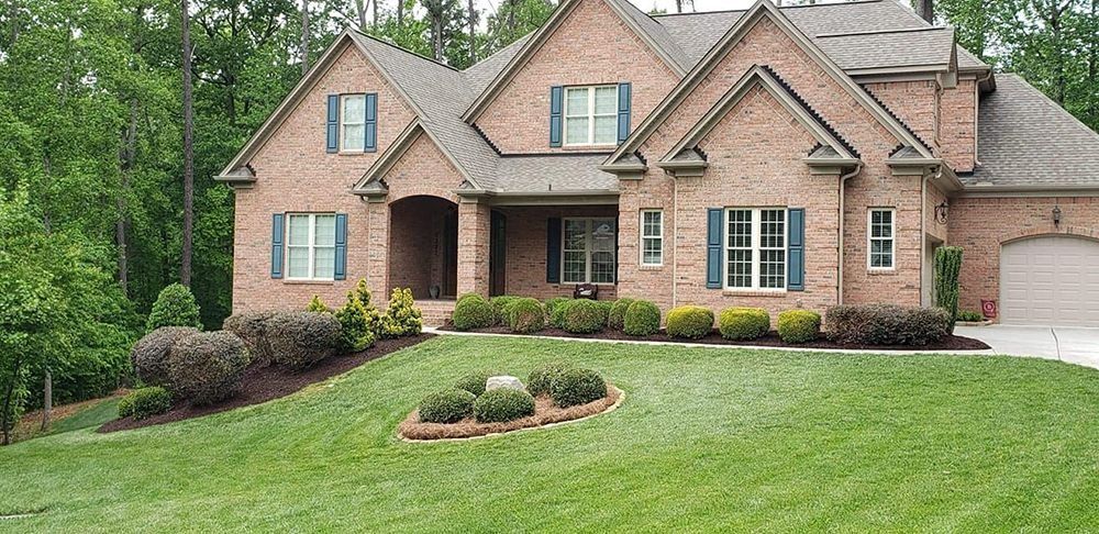 Brick house with green lawn, landscaping, and trees in the background.