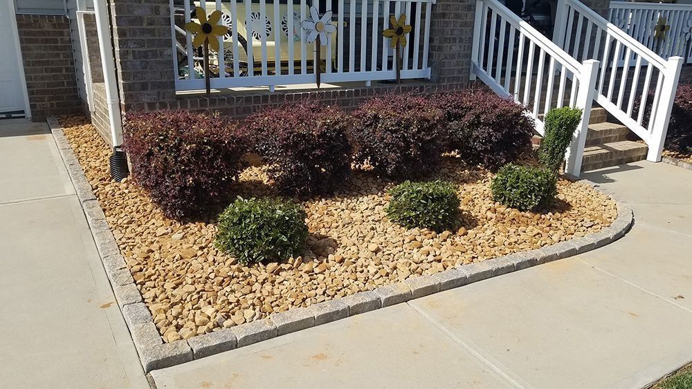 Landscaped front yard with red and green bushes, bordered by tan stone and concrete.
