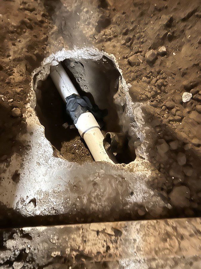White and tan PVC pipes connected in a dirt pit, sealed with black tape.