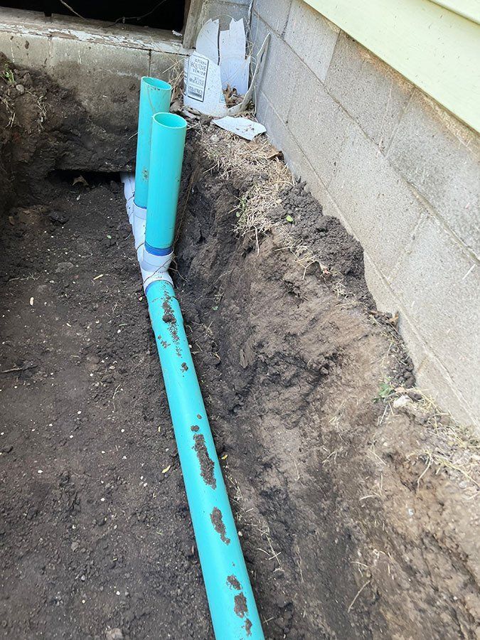 Trench with turquoise pipes installed near a building's foundation, ready for drainage.