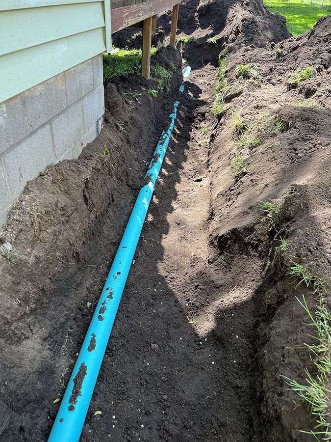 A blue drainage pipe installed in a trench next to a house foundation and under a deck.