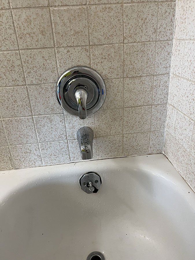 Bathtub with chrome faucet and shower head on tiled wall.
