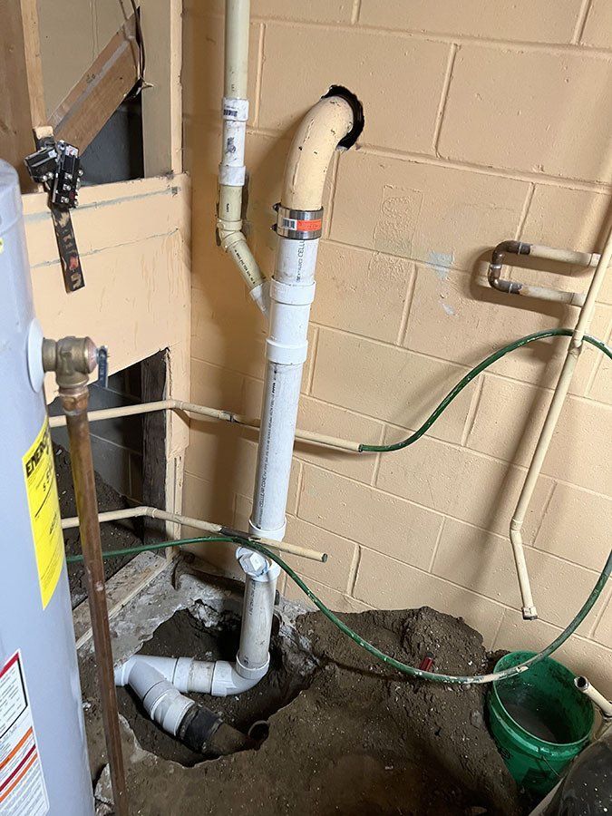 Plumbing pipes in a basement. White and tan pipes connect to a drain. The wall is light brown.