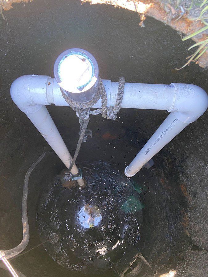 PVC pipe frame over a dark, round object in a hole, possibly a septic tank; rope visible.