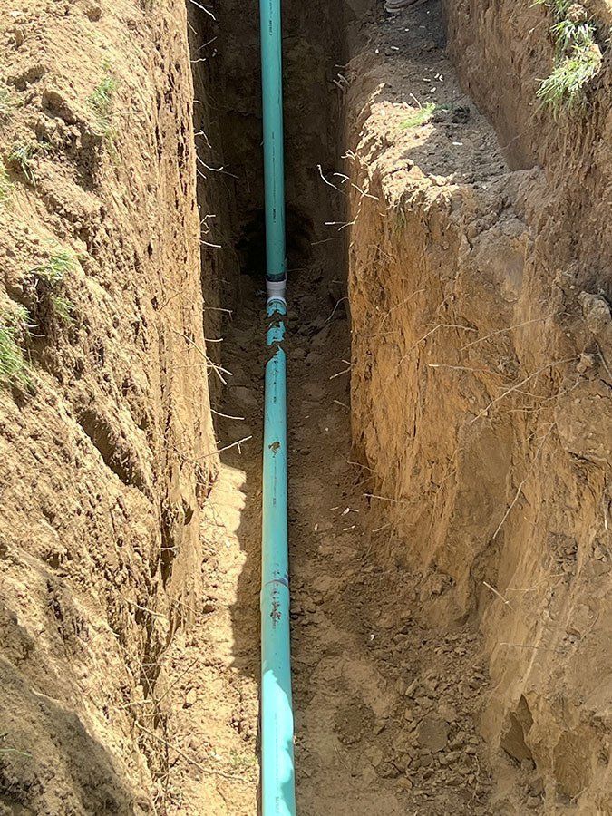 A trench in dirt with turquoise pipe running through it.