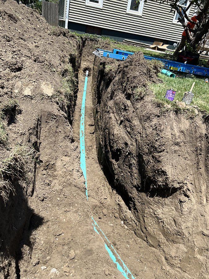 Long trench in dirt, containing blue piping; construction site, outdoors.