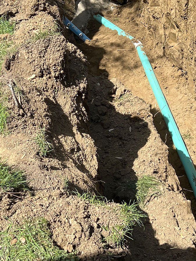 A trench dug in dirt, showing a turquoise pipe angled through the soil.
