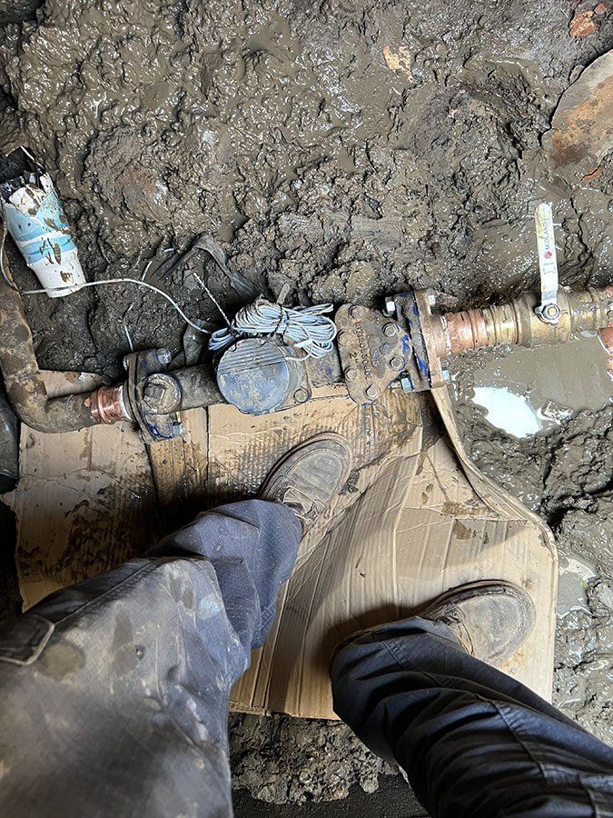 Person standing near water pipe in muddy ground, possibly a repair job.
