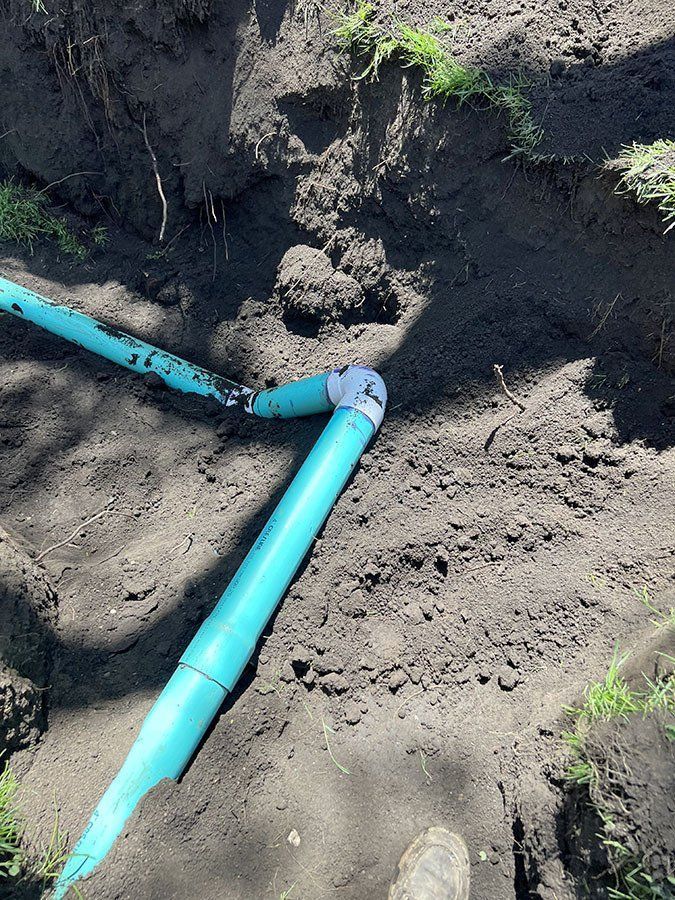 Blue PVC pipes and elbow fittings in a dug trench.