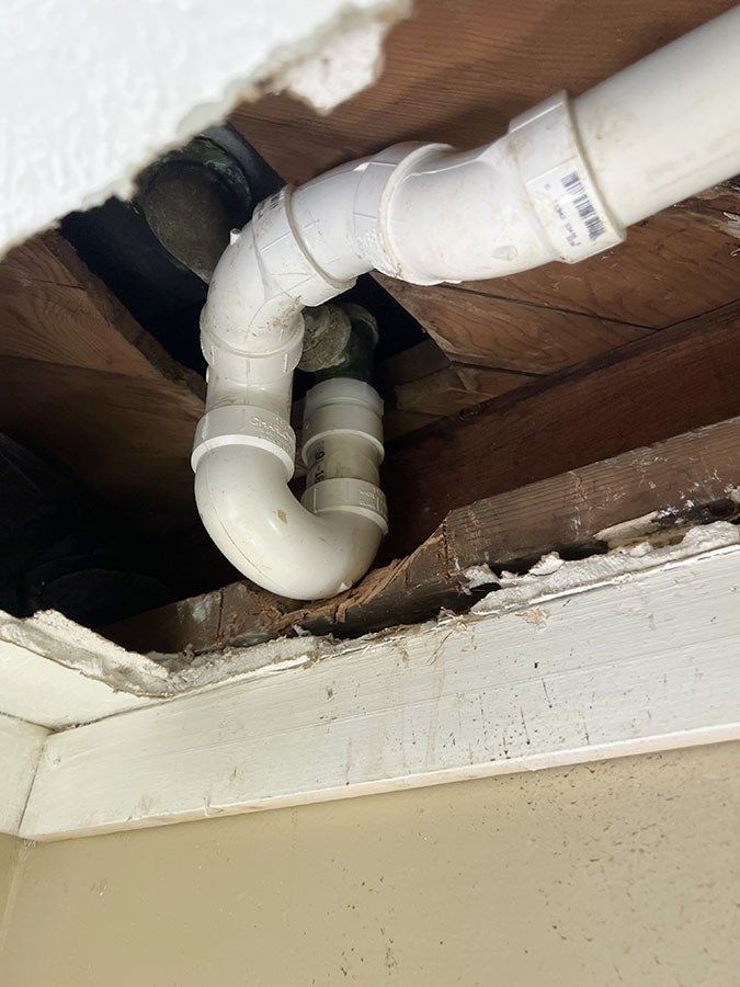 White PVC pipes with a U-bend in a ceiling opening. Wooden beams surround the pipes.