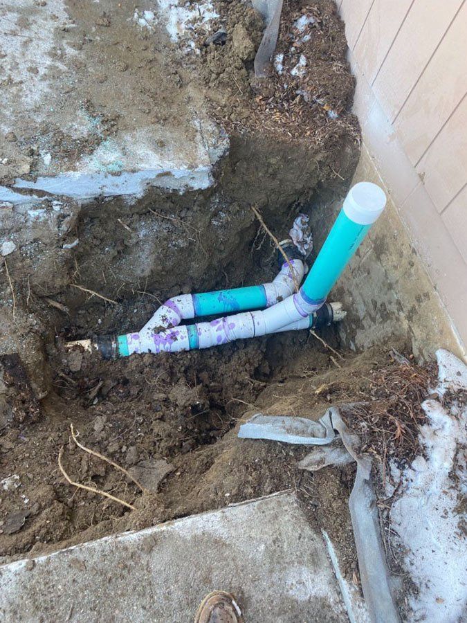 Plumbing pipes in a dirt hole, partially buried. Green and white pipes connect in Y-shaped configuration.