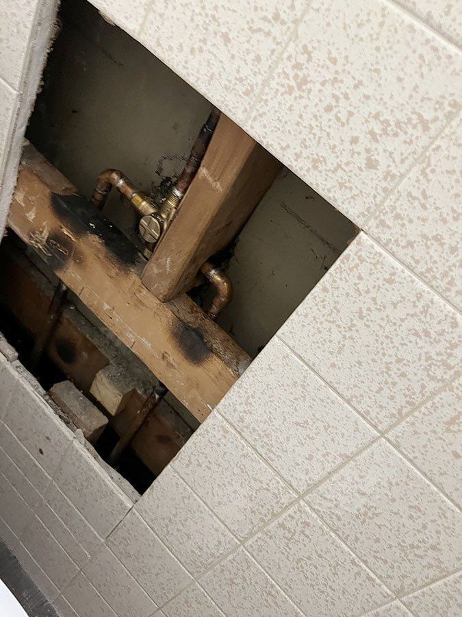 Ceiling tile removed, revealing charred wood beams and copper plumbing.