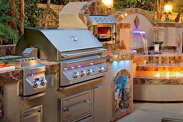A stainless steel grill is sitting in a kitchen with a waterfall in the background.