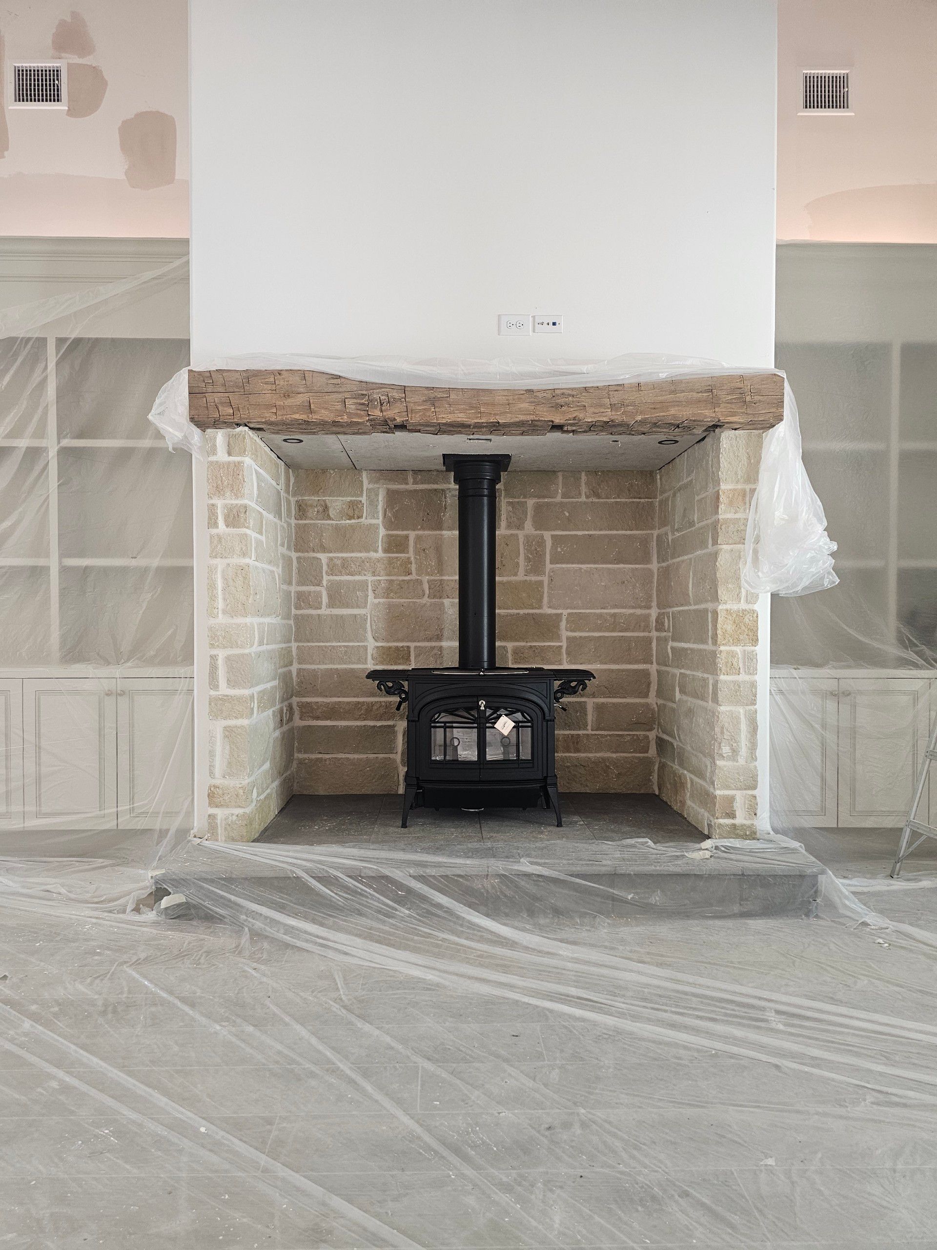 A wood stove is sitting inside of a stone fireplace.