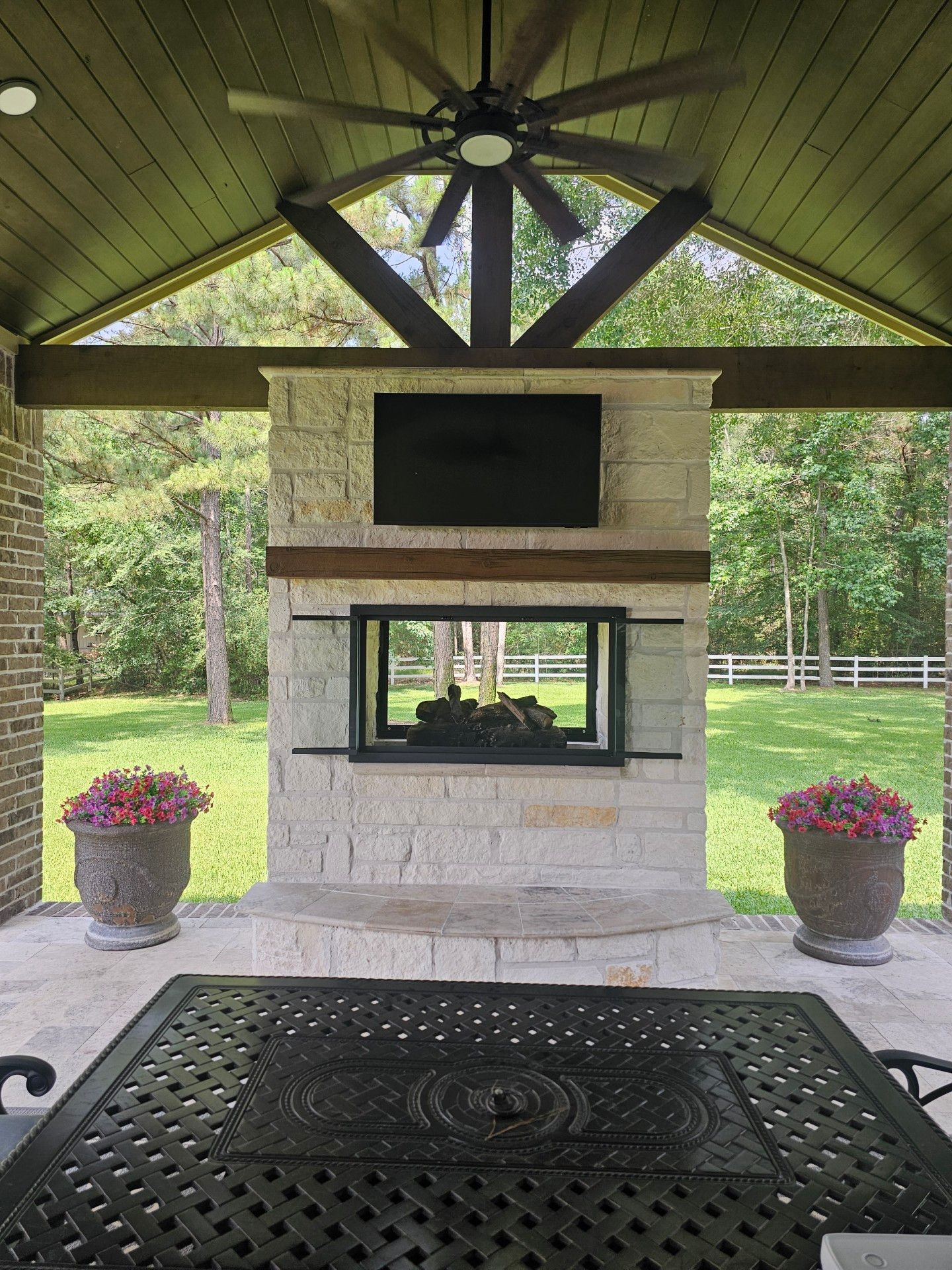 A patio with a fireplace , table , chairs and a ceiling fan.