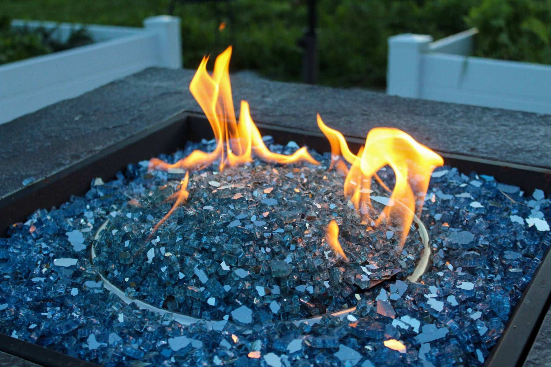 A fire pit with blue glass rocks and flames coming out of it.